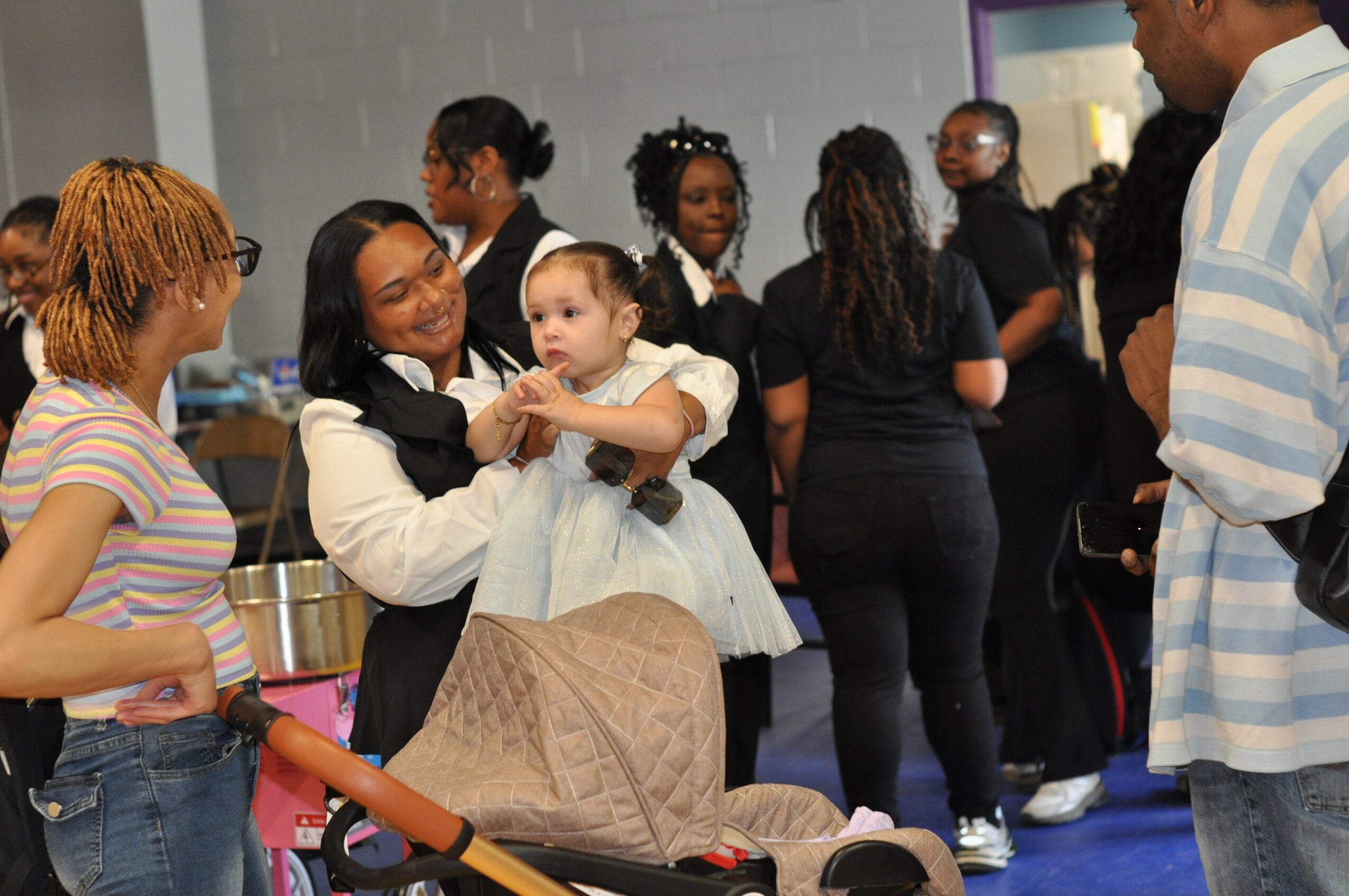 Group of people, including a woman holding a young girl, in an indoor setting with others in the background.