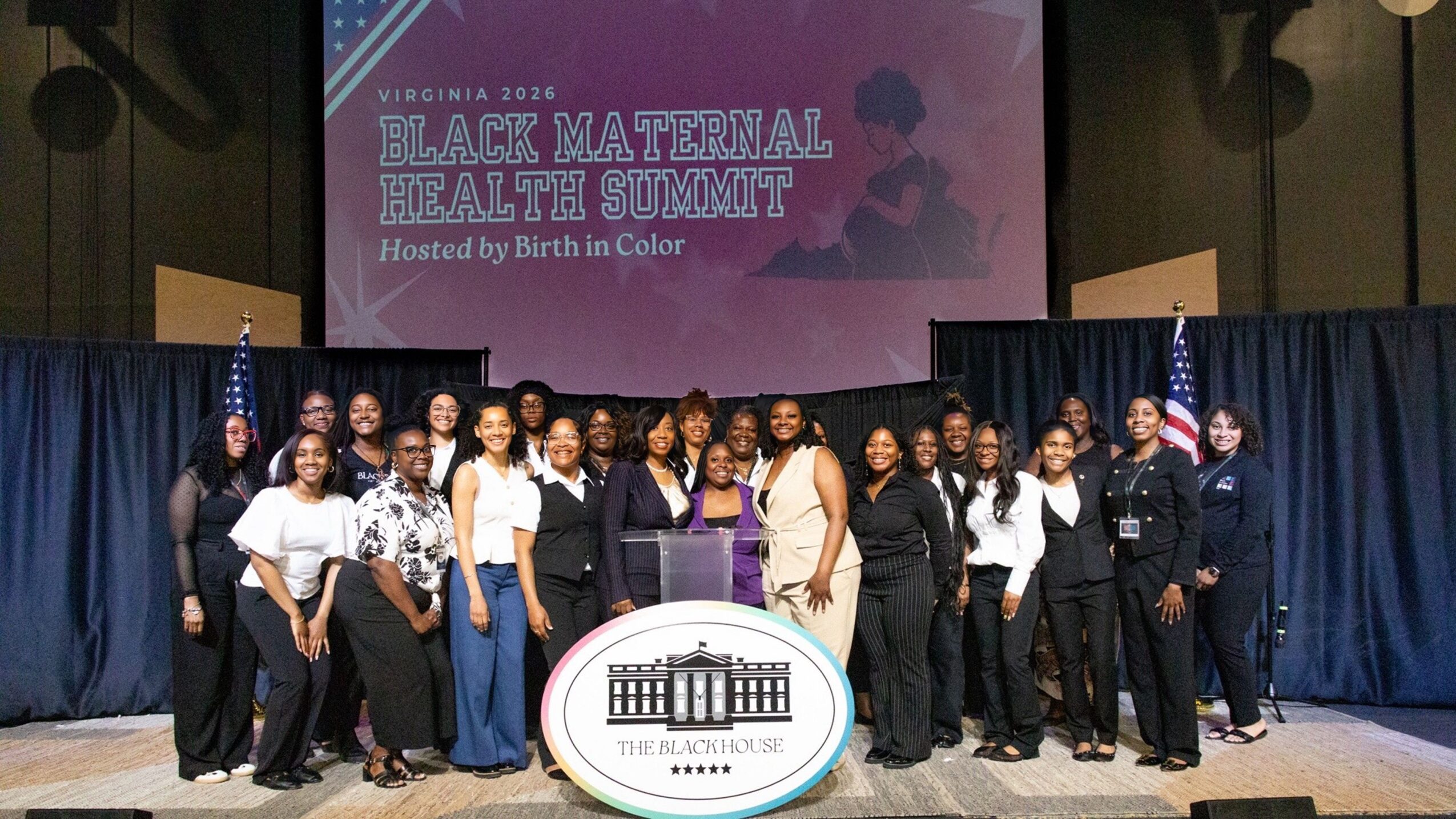 Group of people on stage at Black Maternal Health Summit, with a screen and logo behind them.