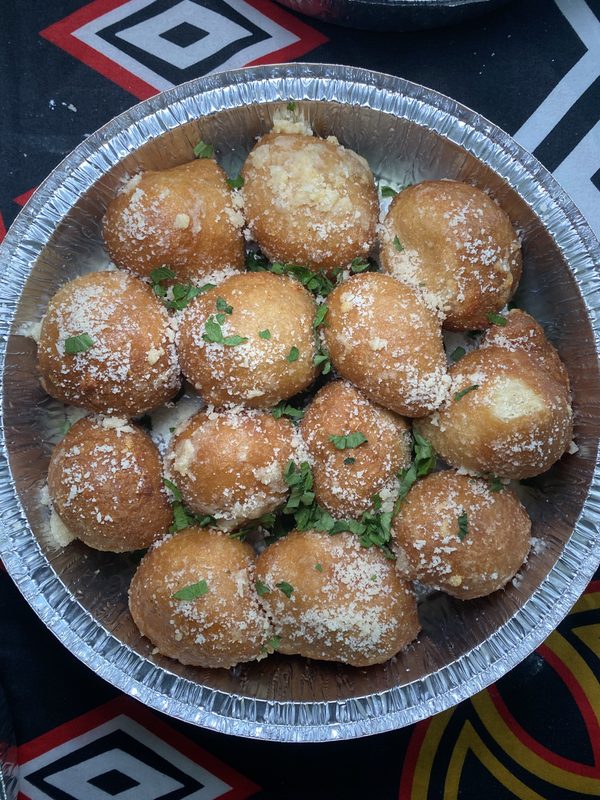 Round fried snacks sprinkled with sugar and garnished with green herbs in a metal tray.