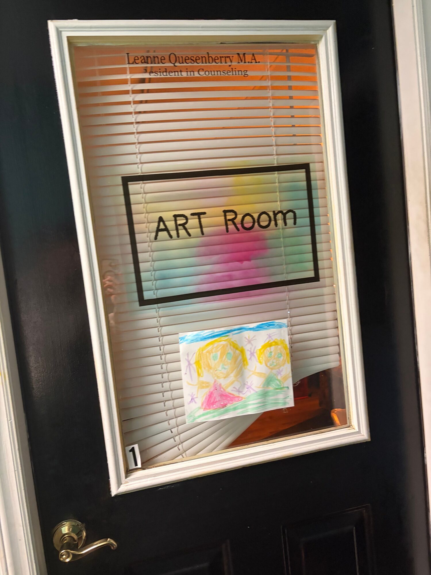 Door with a window displaying a sign for ART Room and a colorful drawing inside, with a lock at the bottom right.
