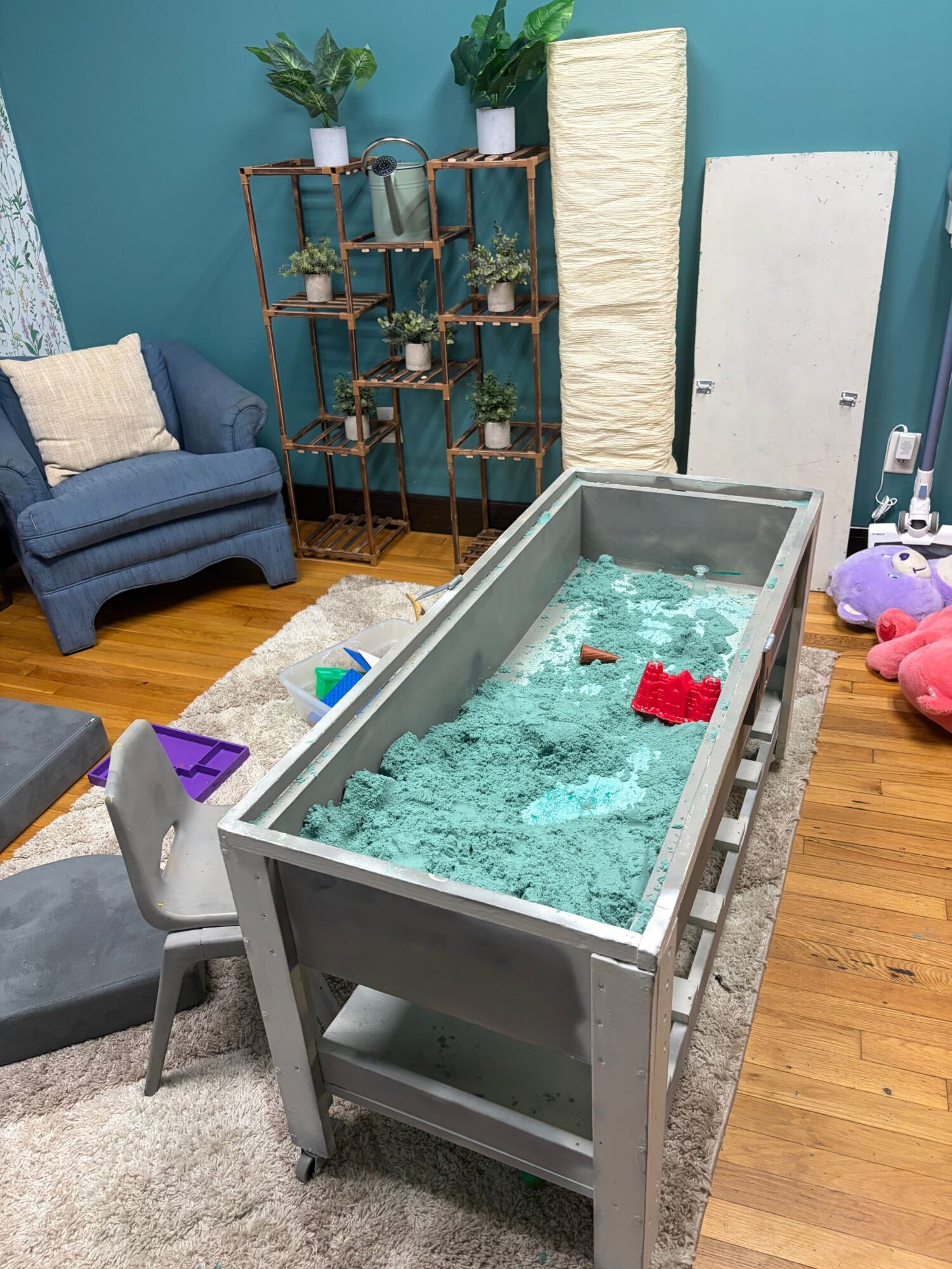 A rectangular glass tank filled with blue shredded paper and red objects, placed on a wooden floor with furniture nearby.