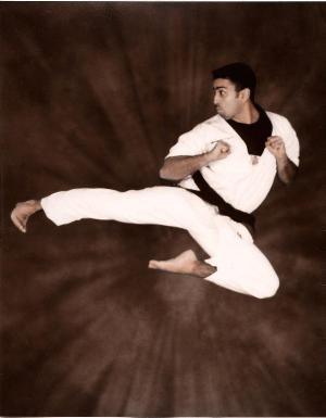 Person in martial arts uniform performing a high jump kick against a dark background.