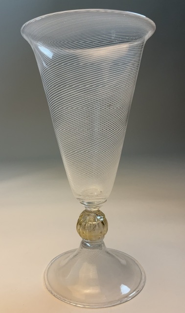Clear glass vase with a flared top, narrow middle, and round base, featuring a decorative gold-colored band, on a neutral background.