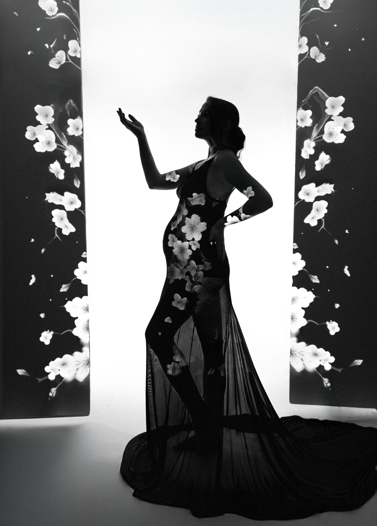 Silhouette of a woman in a long dress with floral patterns, standing with one hand raised, against a bright background with floral designs.