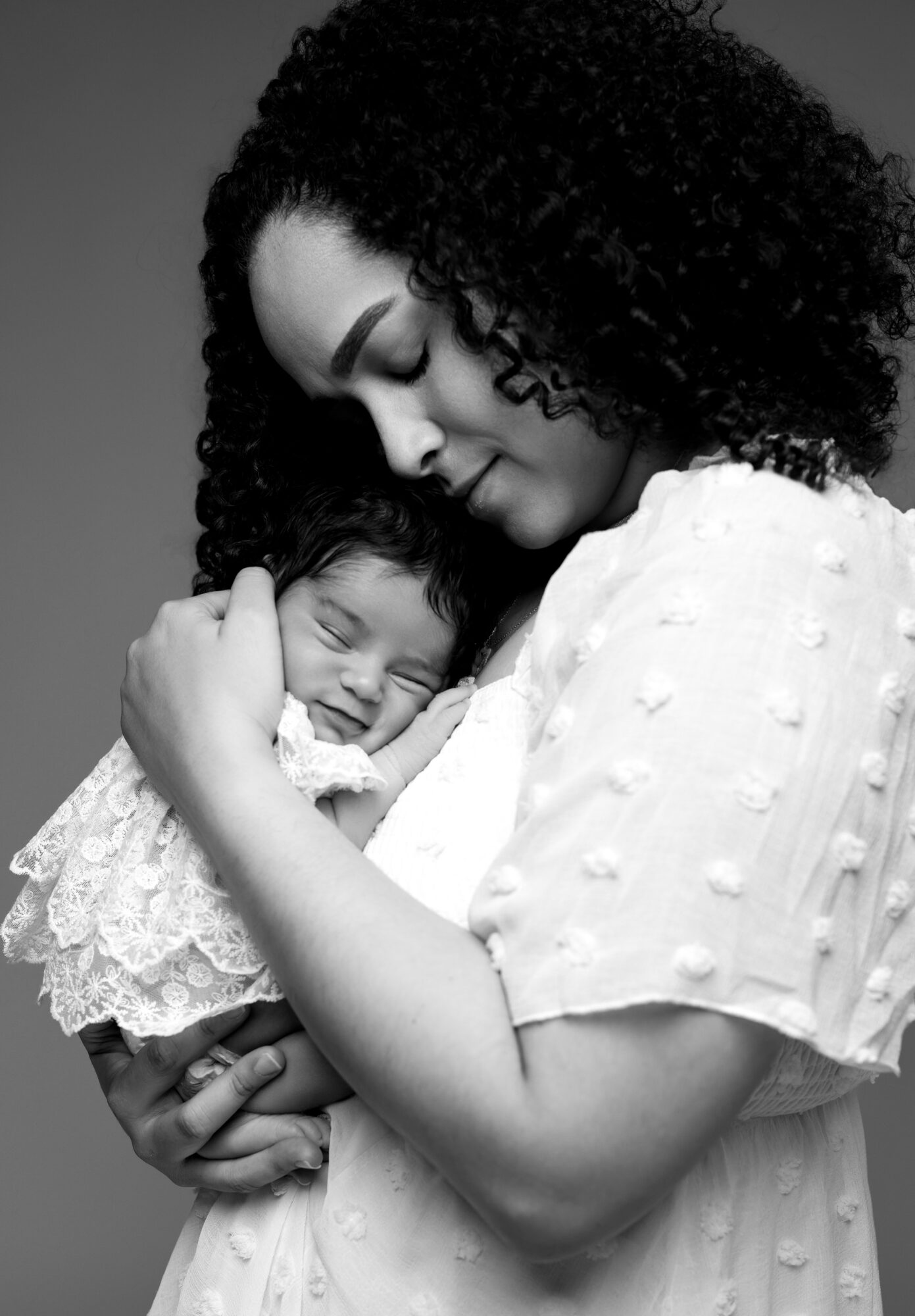 Woman holding a smiling baby close, both with closed eyes, in black and white.