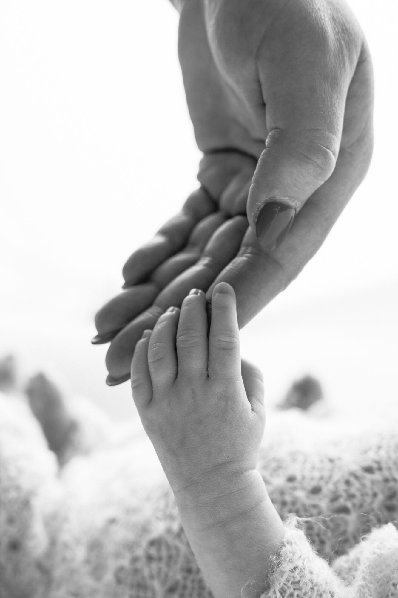 Adult hand gently holding a child's hand, both reaching upward, in black and white.