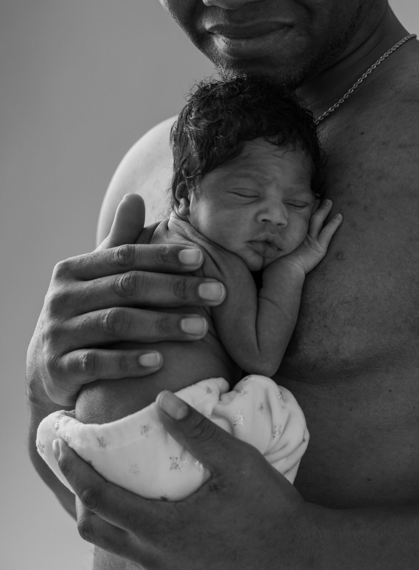 Adult holding a newborn baby close, baby's face resting on hand, in black and white.