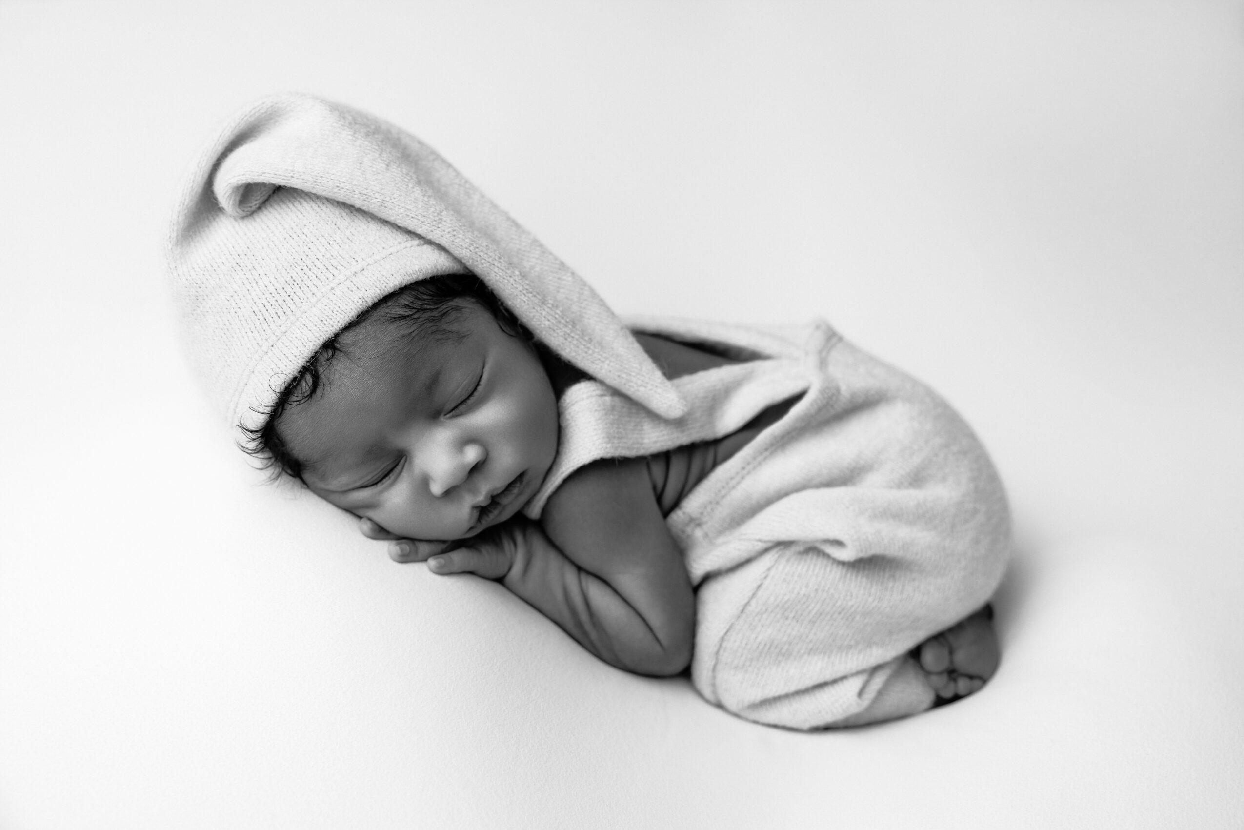 Newborn baby sleeping, wearing a hat and wrapped in a blanket, lying on a white surface.