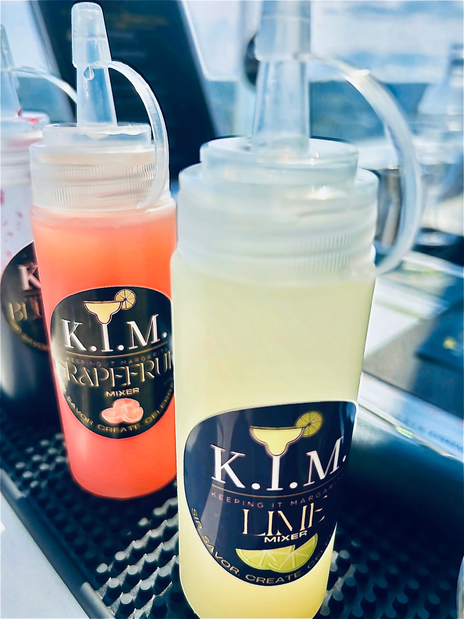 Two mason jar-style drink containers with straws, one pink and one yellow, on a black surface with a blurred background.