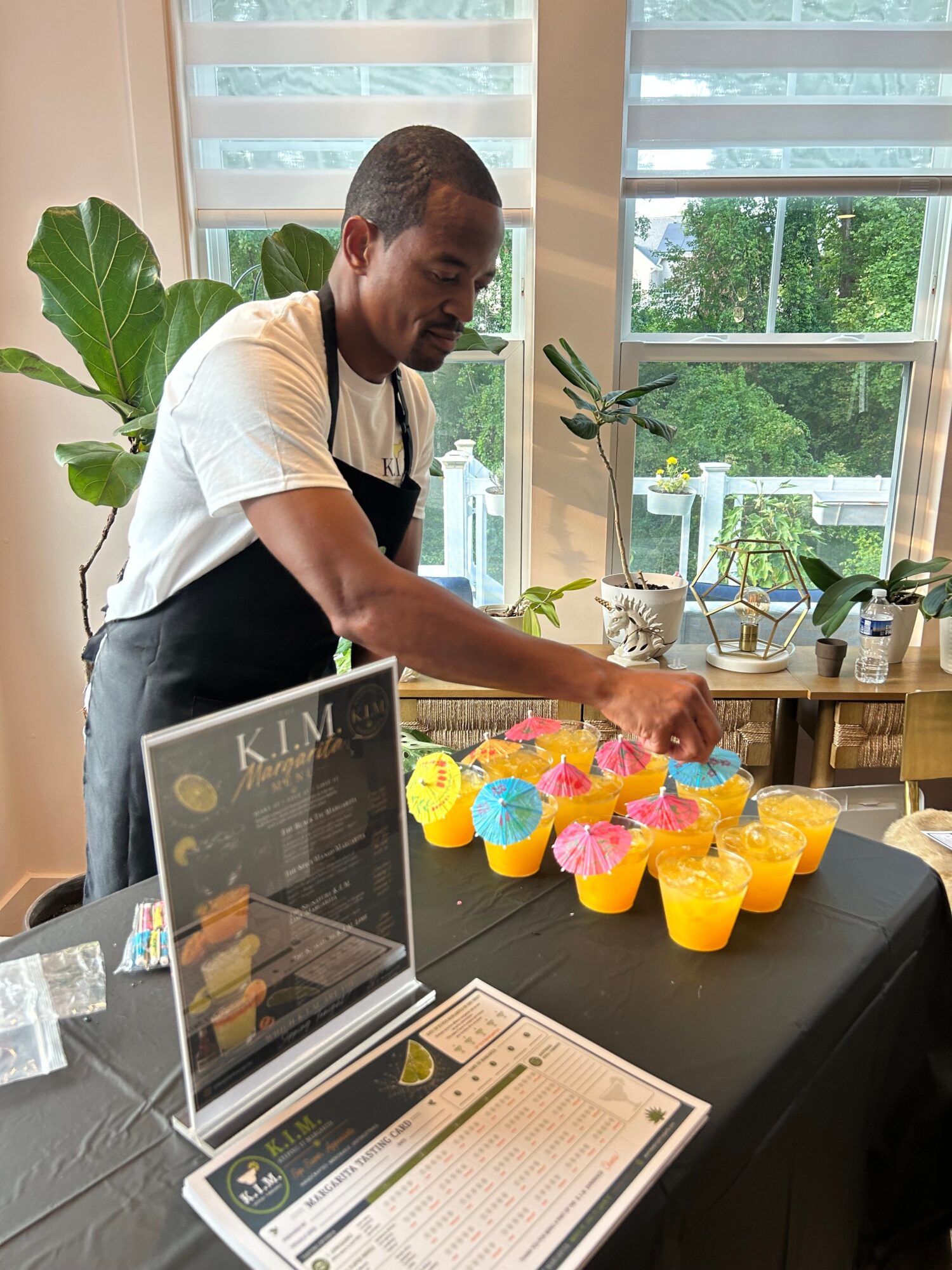 Person arranging colorful paper cups on a table with a window and greenery in the background.