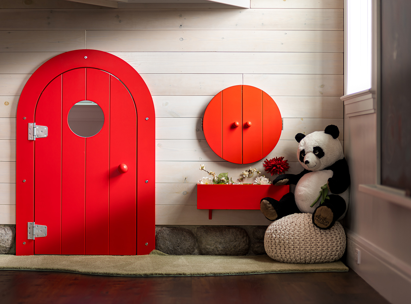 Red door with a circular window, orange wall cabinet, and a panda plush toy sitting on a beige cushion.