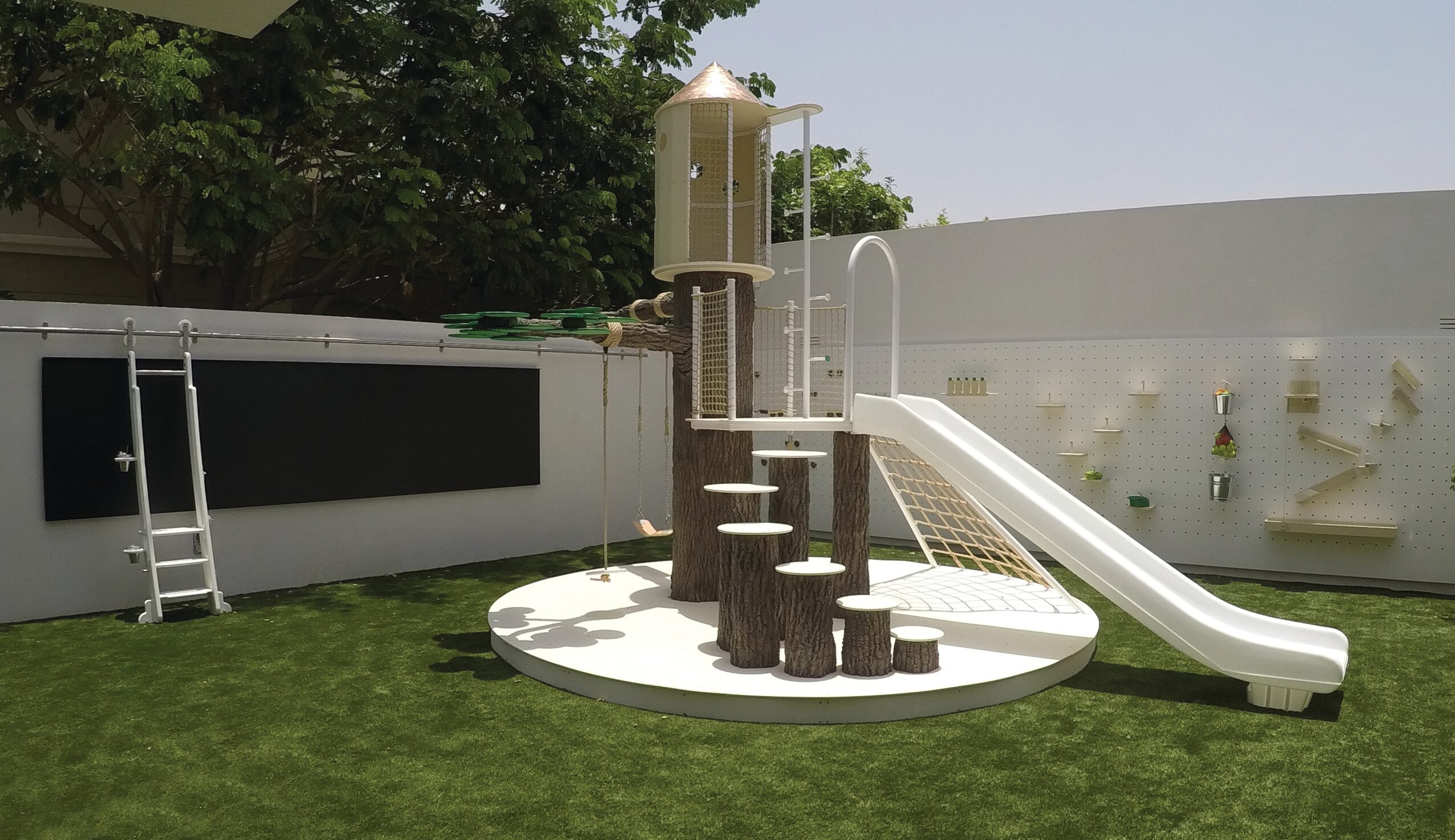 Play structure with a slide, ladder, and climbing steps on a grassy yard, enclosed by a white fence.