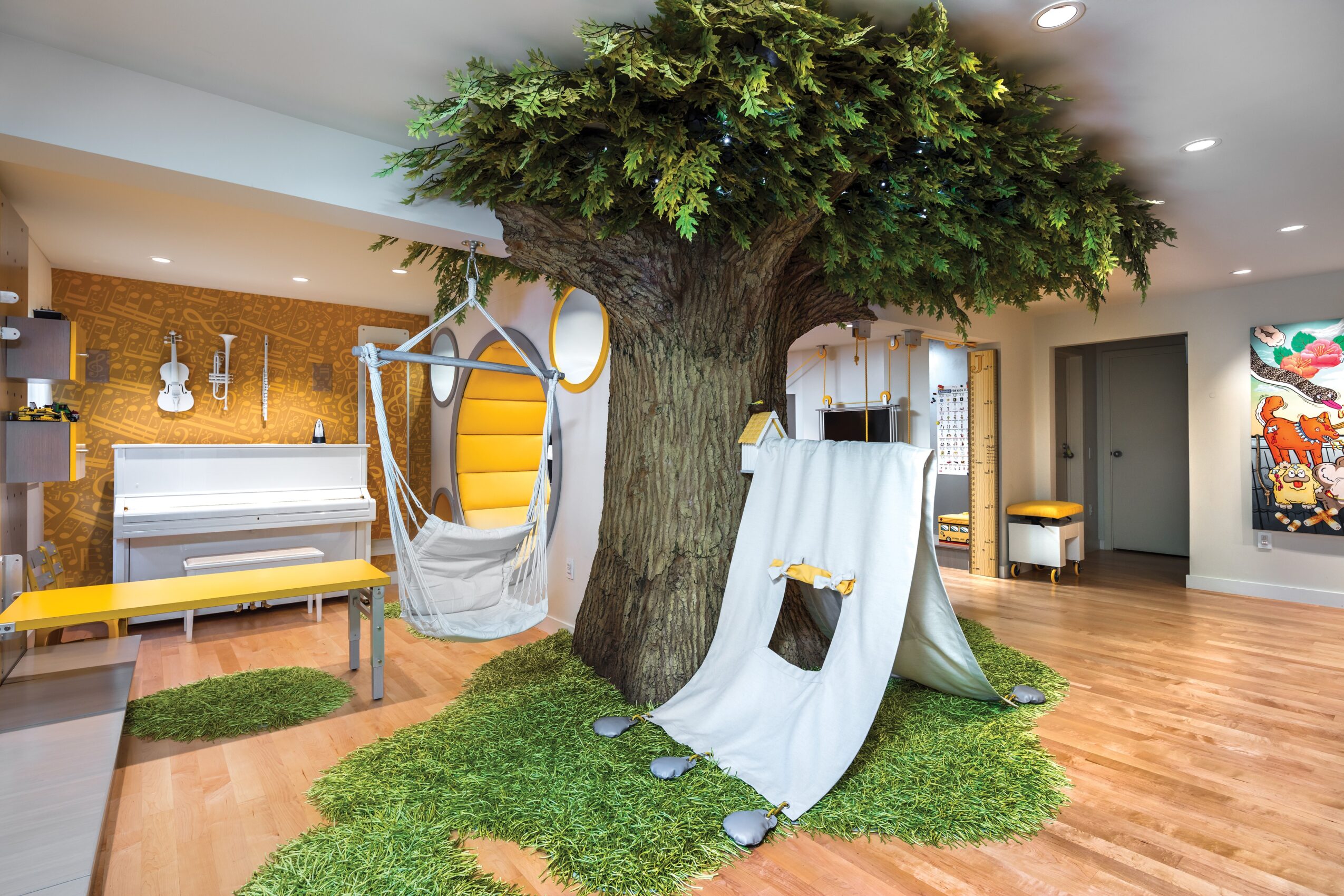 Indoor space with a large tree, swings, and a grassy area, surrounded by furniture and artwork.