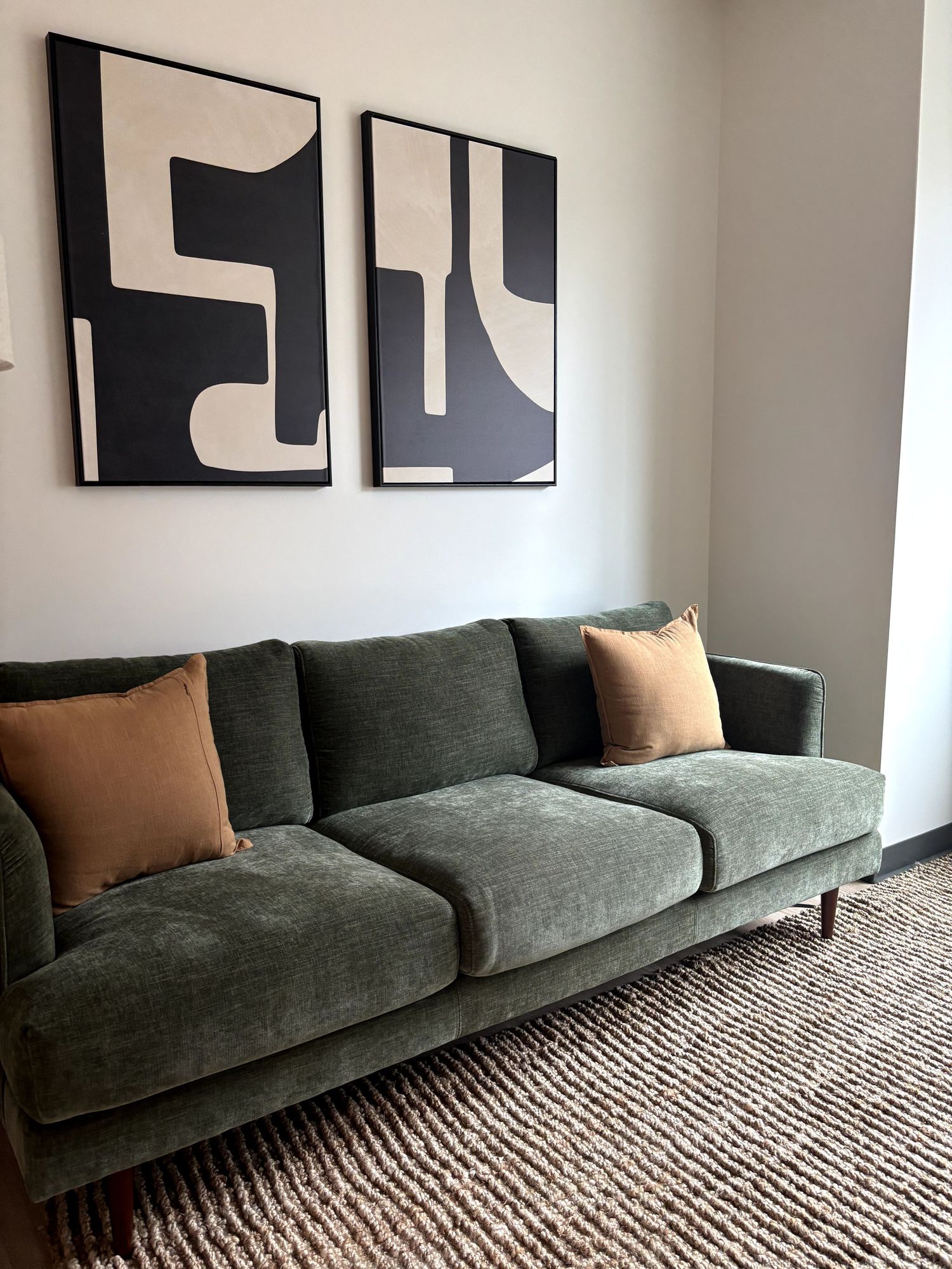 Green sofa with two beige pillows, abstract black and white artwork on wall, neutral-colored room.