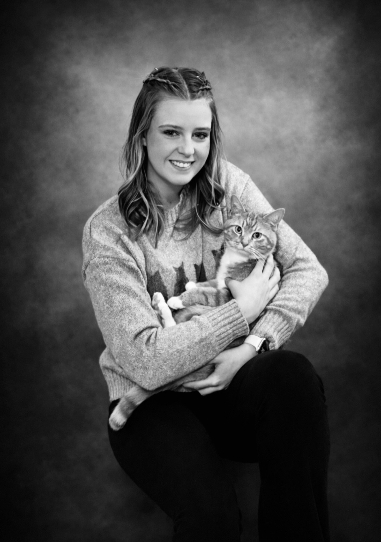 Young woman smiling while holding a cat, sitting against a plain background.