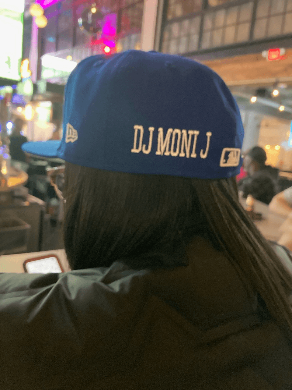 Person wearing a blue cap with white text, in a lively indoor setting with colorful lights and people.