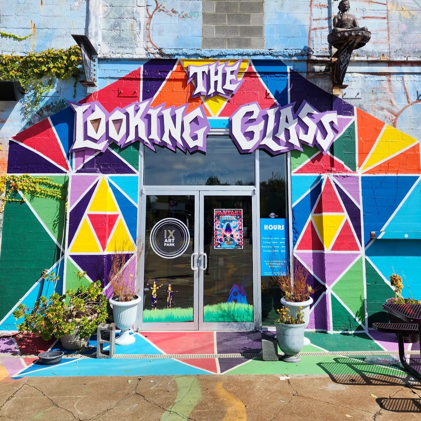 Colorful geometric mural with text 'The Looking Glass' above glass door, plants, and outdoor furniture.