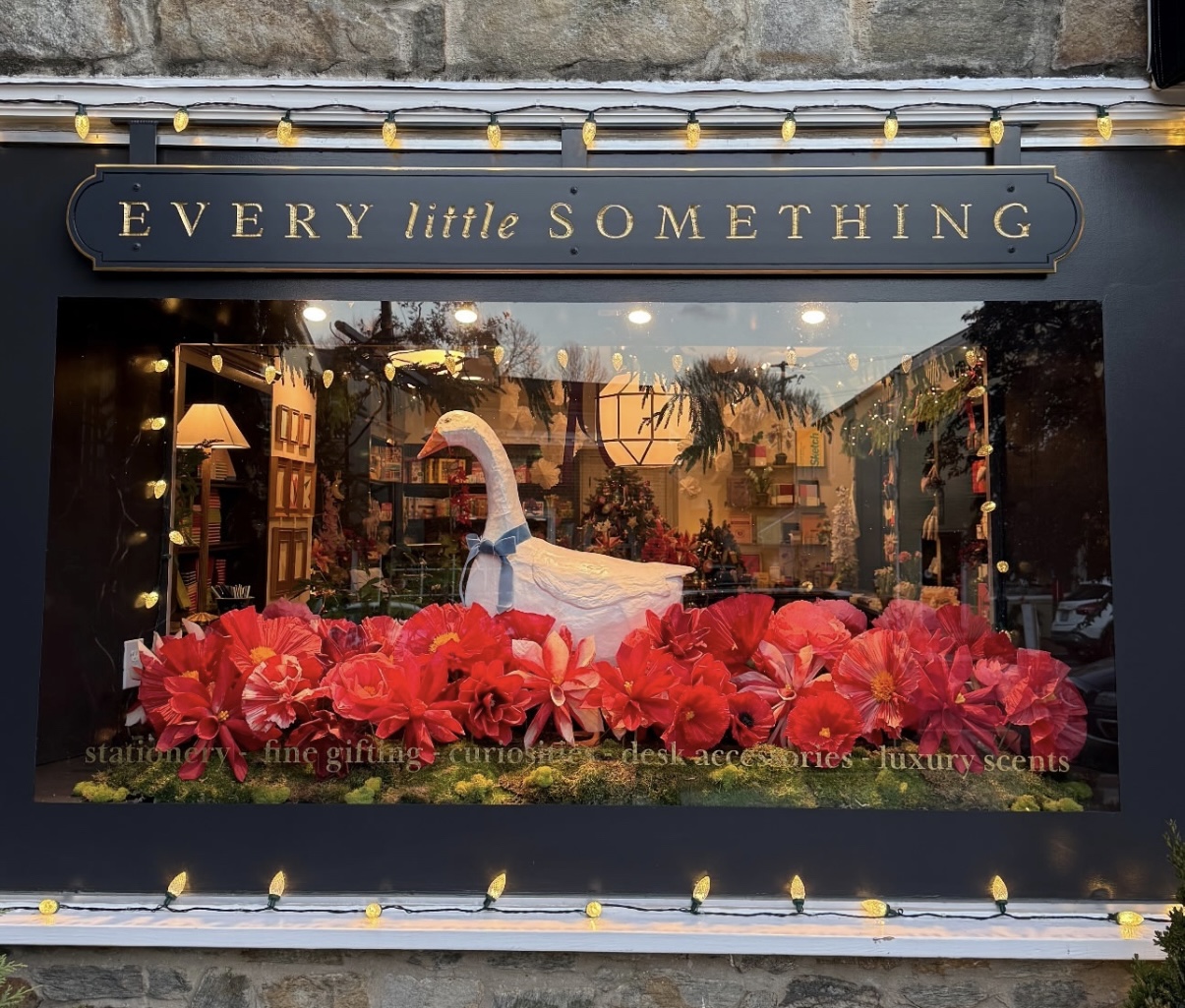 Store window display with a white swan sculpture surrounded by red flowers, and a sign reading 'EVERY little SOMETHING'.