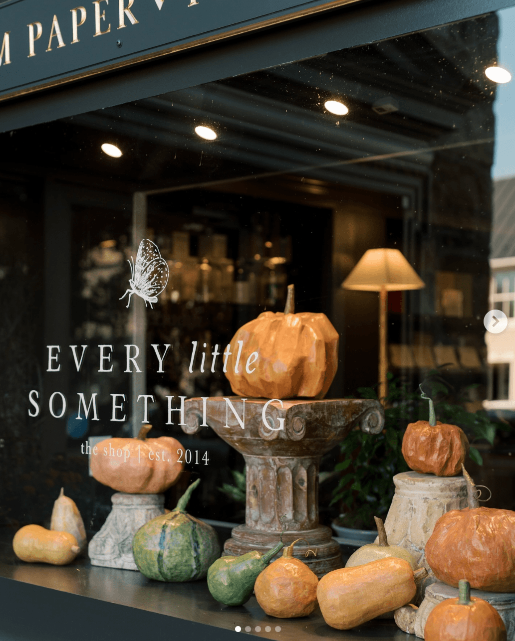 Display of pumpkins and gourds on a window ledge with a pumpkin centerpiece, inside a shop with warm lighting.