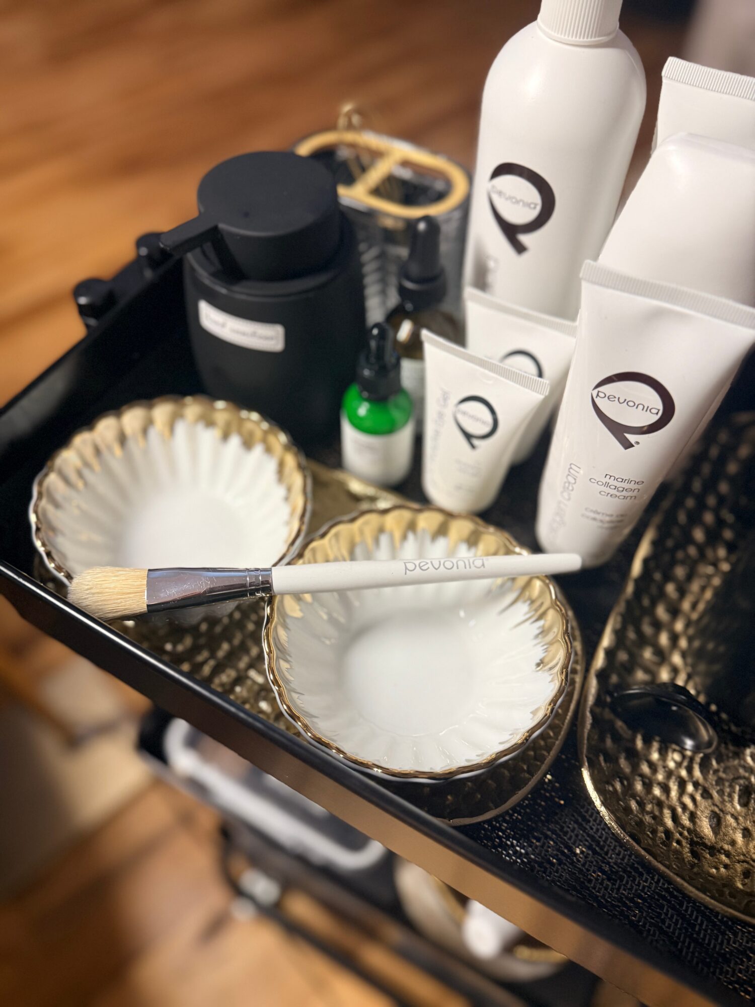 Beauty products and brushes on a black tray with gold accents, placed on a wooden surface.