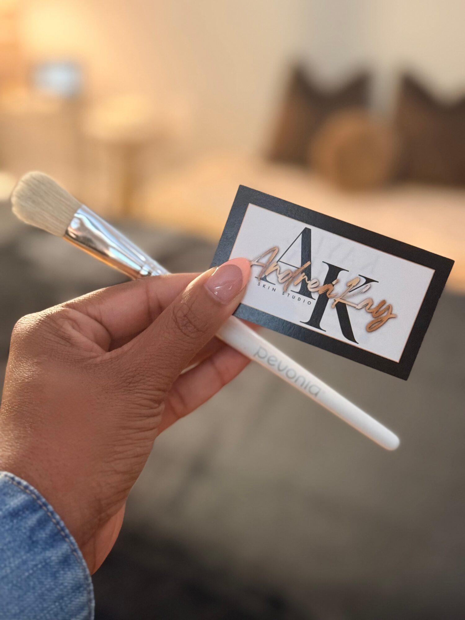 Hand holding a makeup brush and a card with the word 'MAKEUP' in a blurred indoor background.
