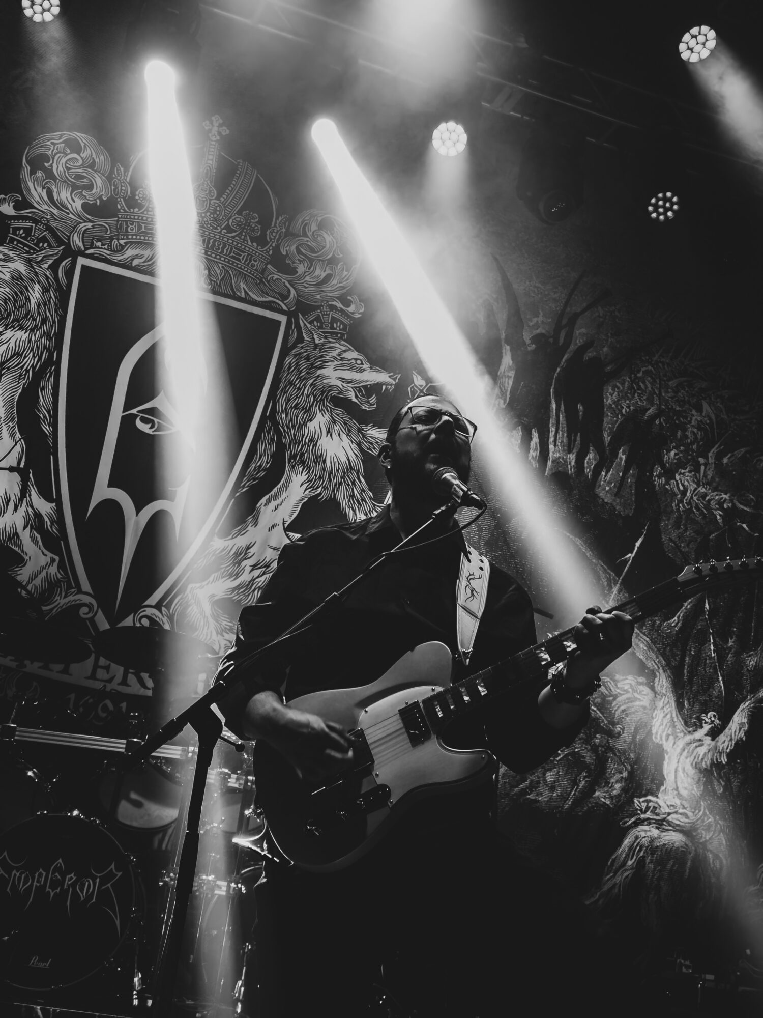 Musician playing electric guitar on stage with dramatic lighting and artistic backdrop, black and white image.