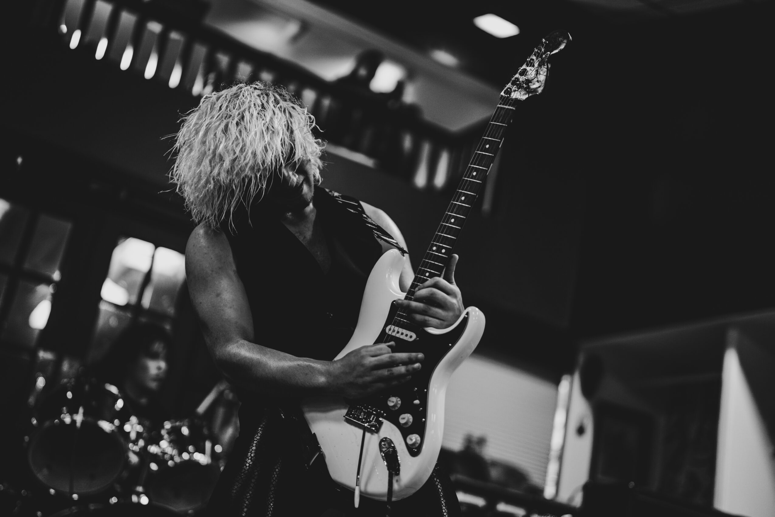Person with curly hair playing an electric guitar on stage in black and white.