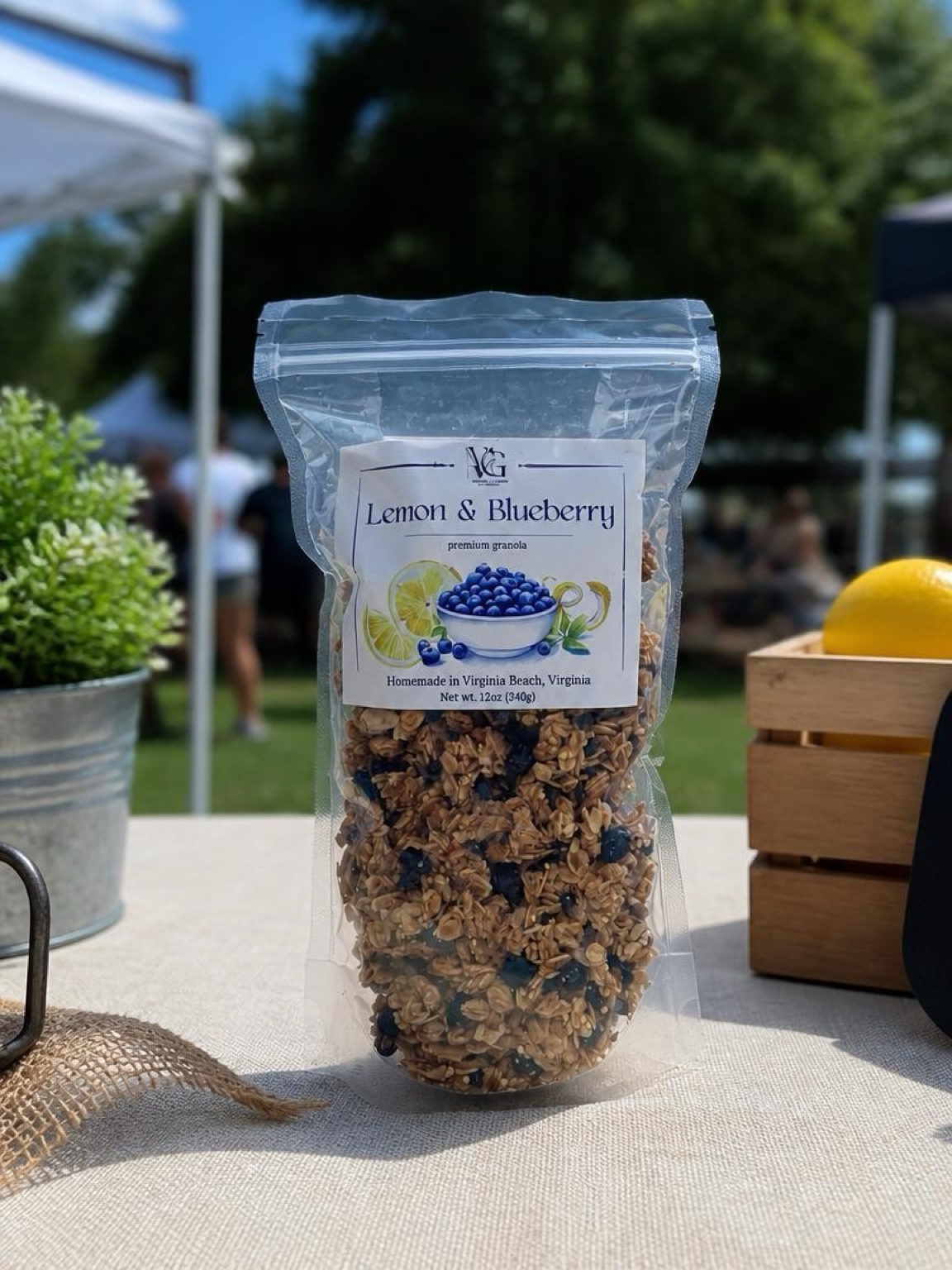 Clear plastic bag of lemon and blueberry granola on a table outdoors, with a potted plant and wooden box nearby.
