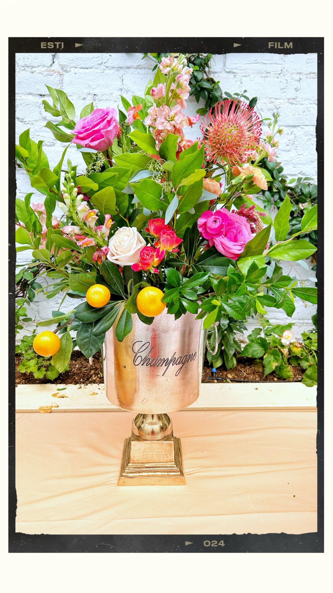Vase with pink, white, and yellow flowers on a wooden surface, with a white brick wall background.