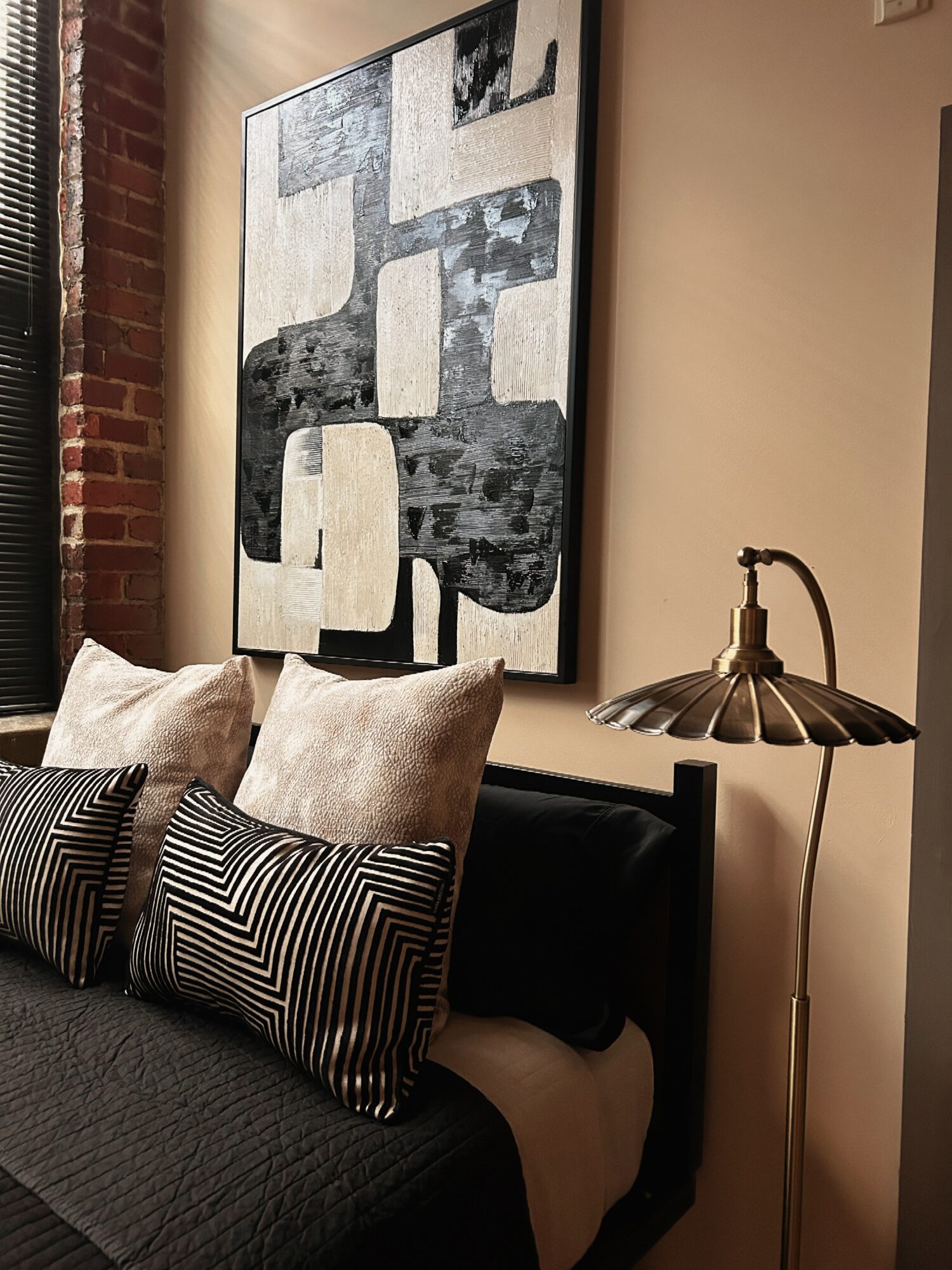 Living room corner with a large abstract black and white painting, beige pillows, and a vintage-style floor lamp.