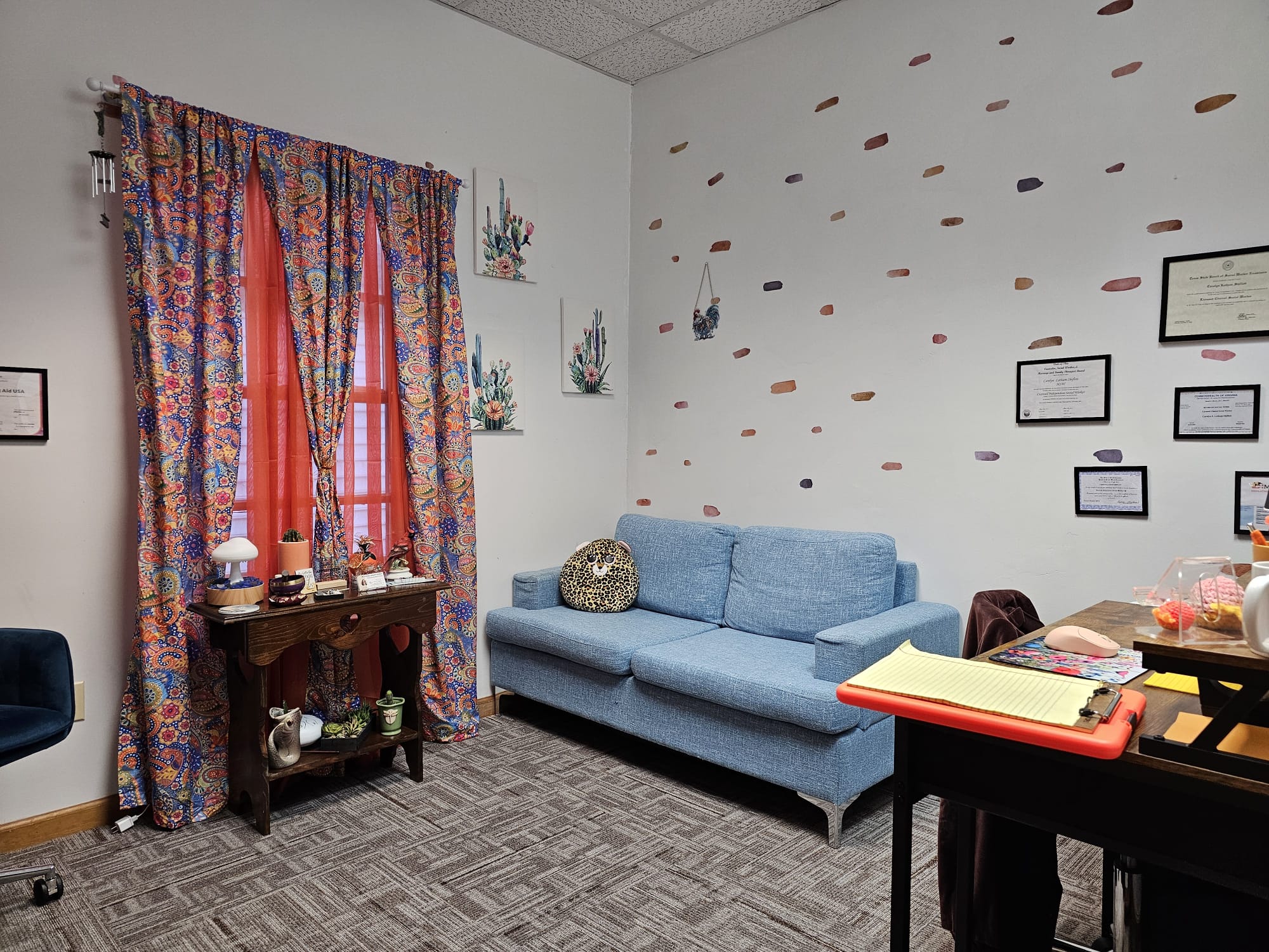Living room with a blue sofa, colorful curtains, wall decorations, and a wooden table with items on it.