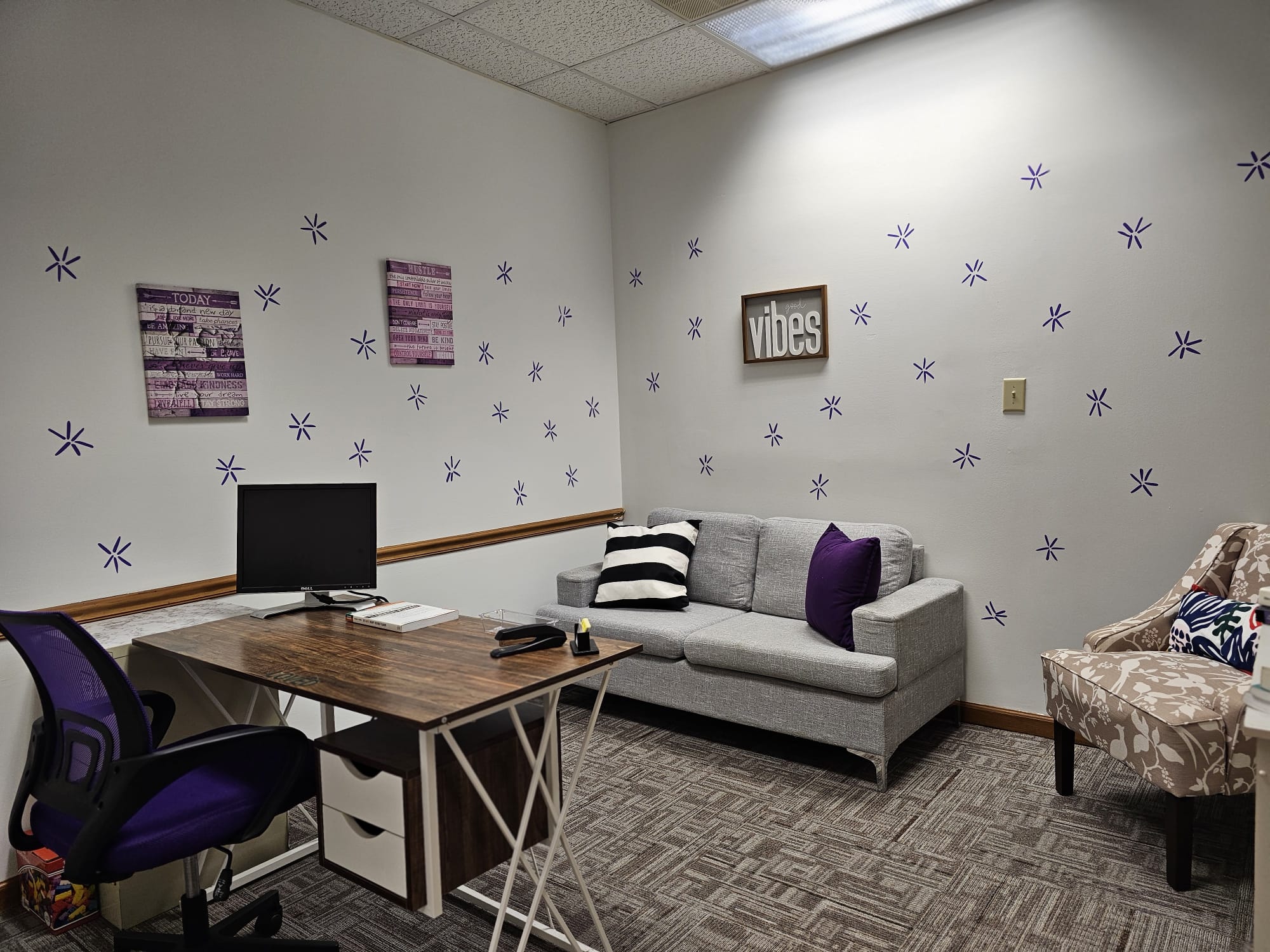 Room with a desk, computer, sofa, and patterned chair, decorated with purple stars and wall art.