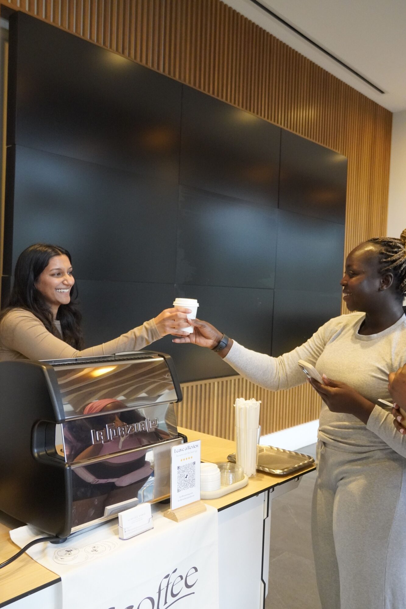 Two women shaking hands in a modern office, with a table, documents, and a black wall in the background.