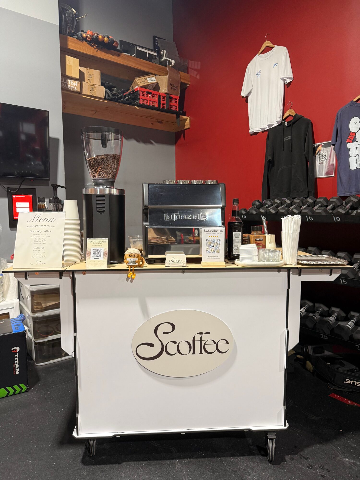 Coffee shop counter with a white So Coffee sign, coffee machine, and various supplies, against a red and gray wall.
