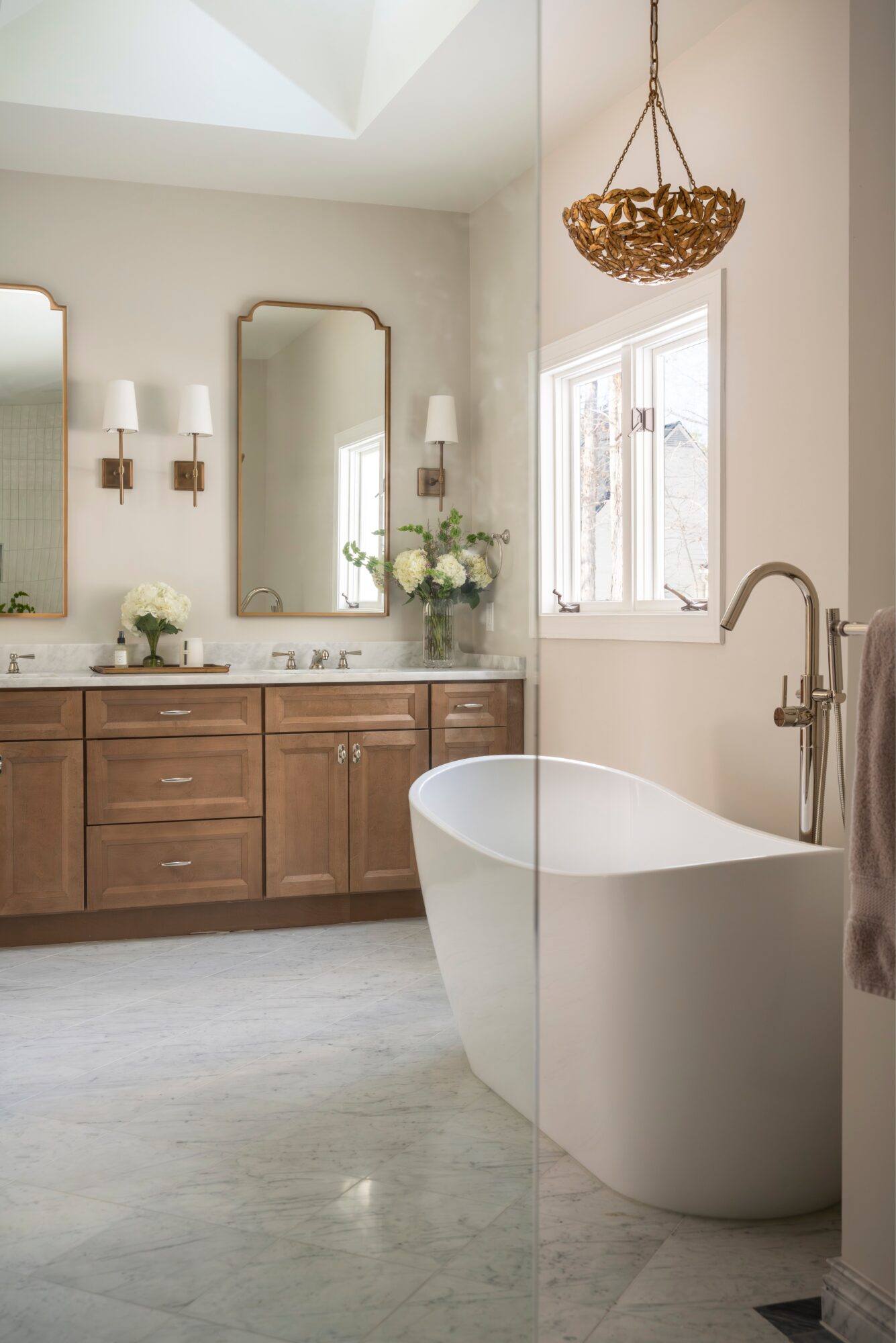 Bathroom with a freestanding bathtub, wooden vanity with two mirrors, and a window with natural light.