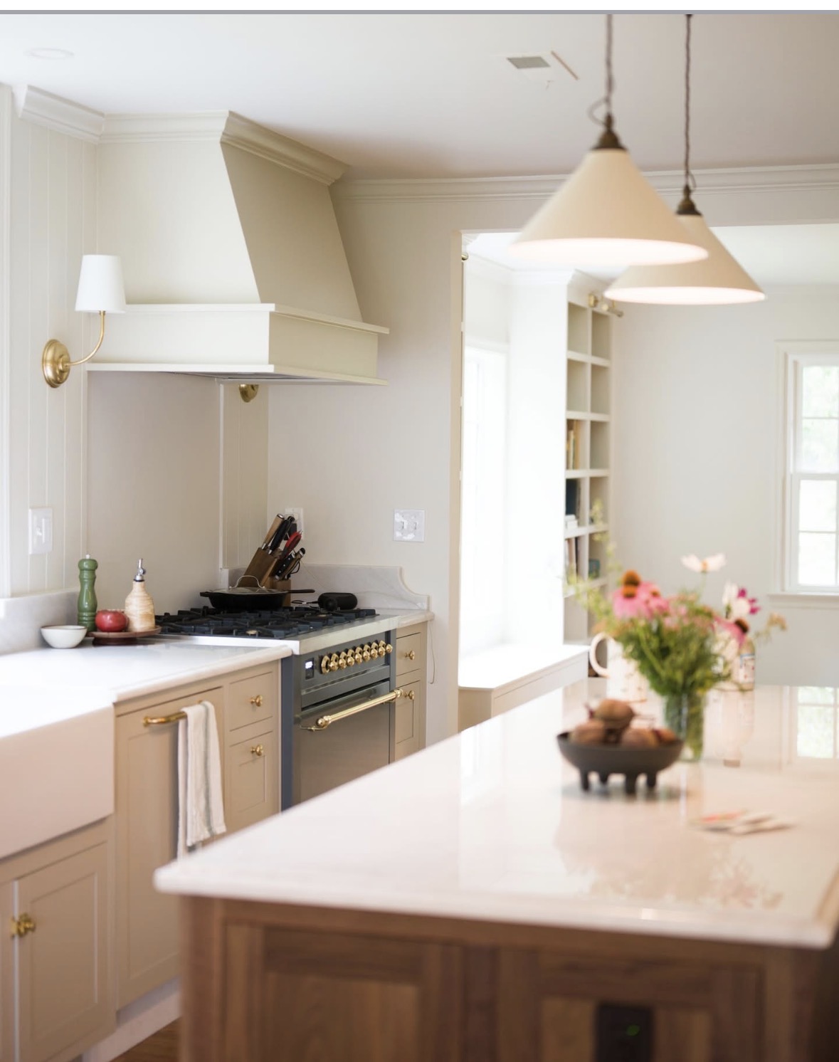 Kitchen with white cabinets, a stove, and a kitchen island with a vase of flowers, pendant lights, and natural light from windows.