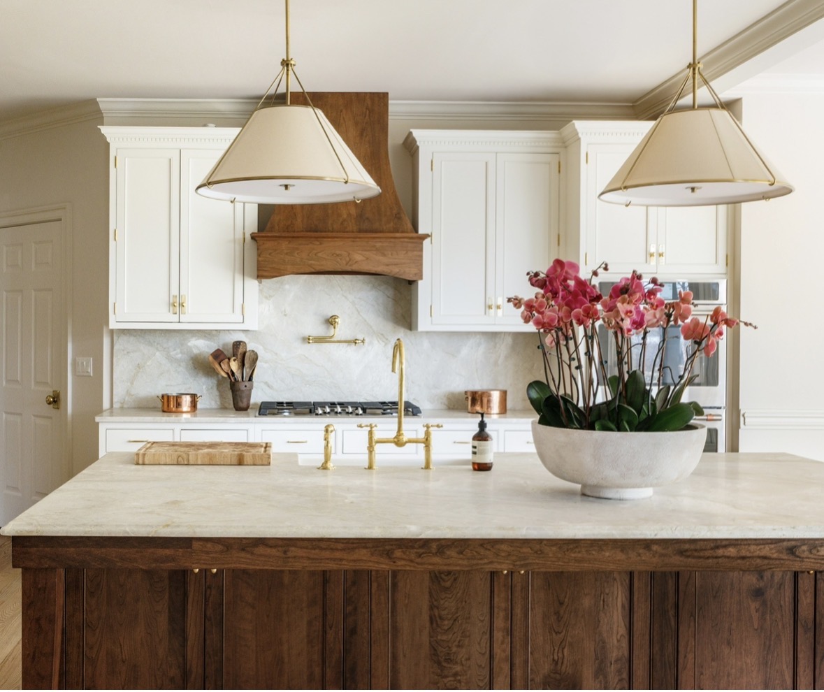Kitchen with white cabinets, a marble backsplash, a wooden range hood, and a large flower pot with pink flowers on the island.