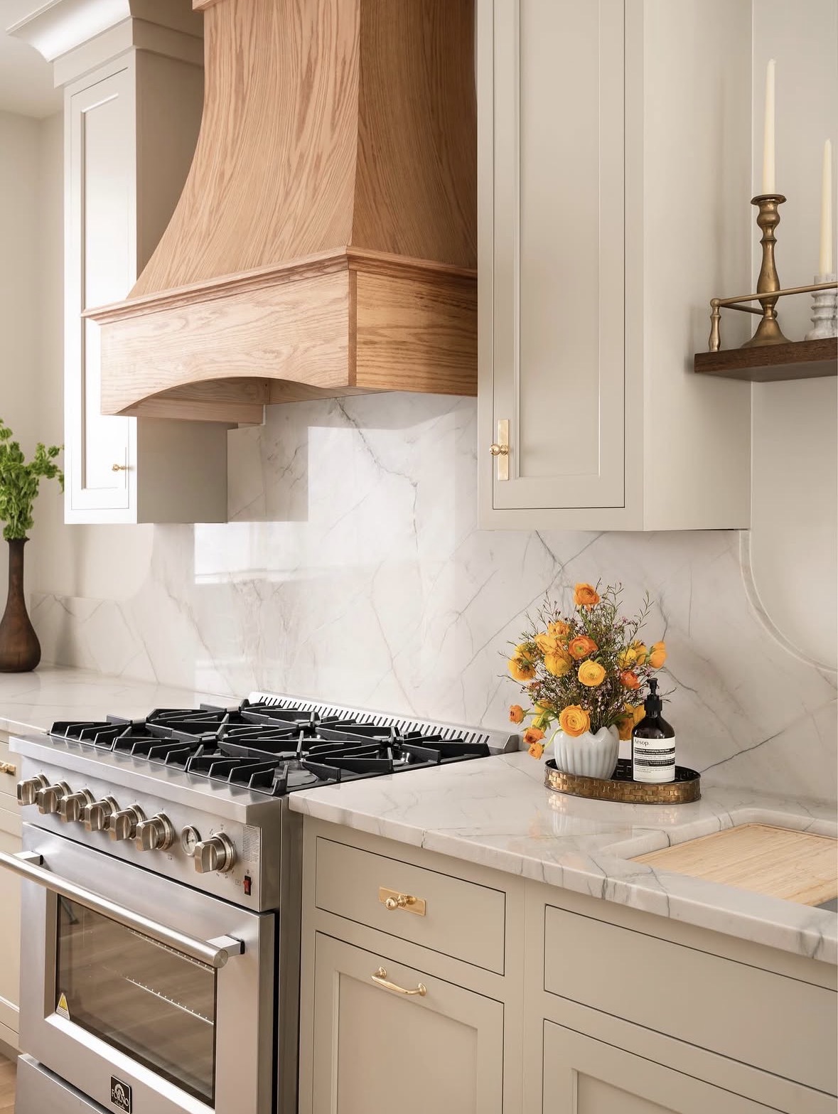Kitchen with beige cabinets, marble backsplash, stove, and a flower arrangement on the counter.