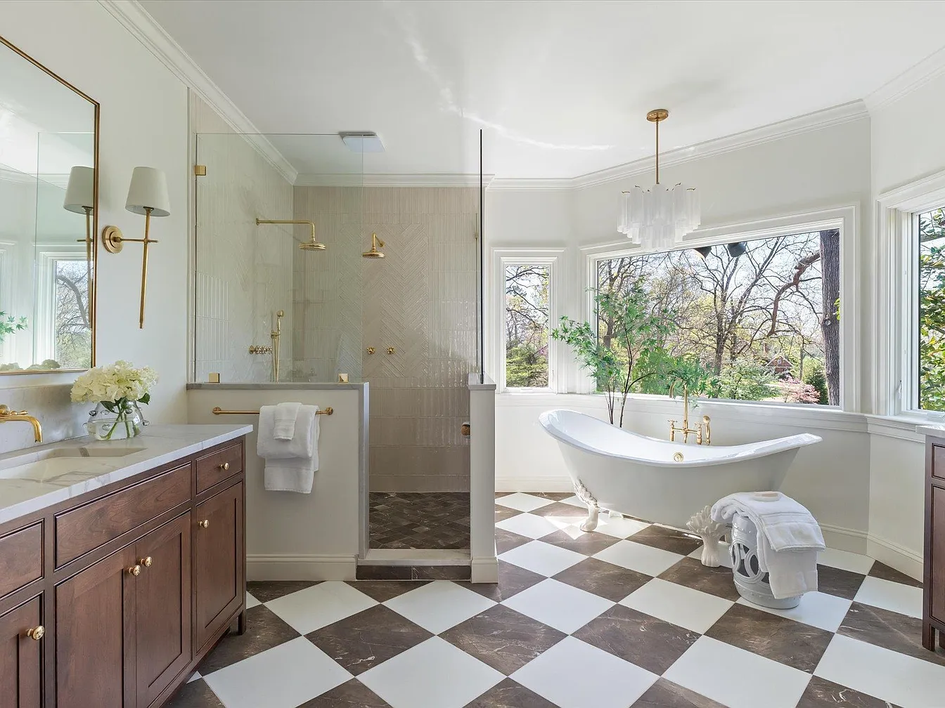 Bathroom with checkered floor, bathtub near windows, glass shower, wooden vanity, and natural light from outside.