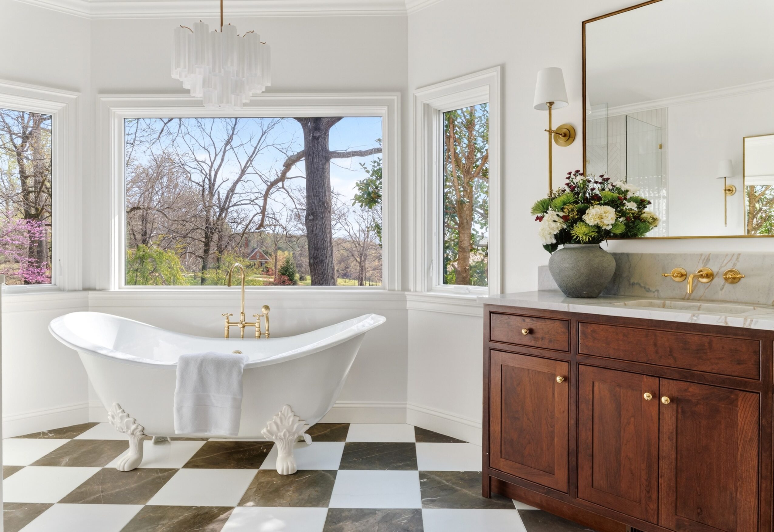 Bathroom with a clawfoot bathtub, large window, wooden vanity, and checkered floor, overlooking trees outside.