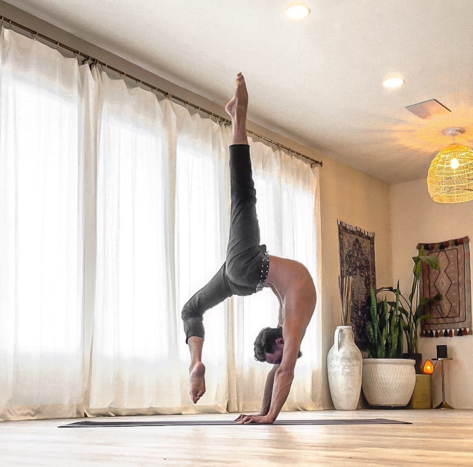 Person performing a handstand in a room with large windows, curtains, and indoor plants.
