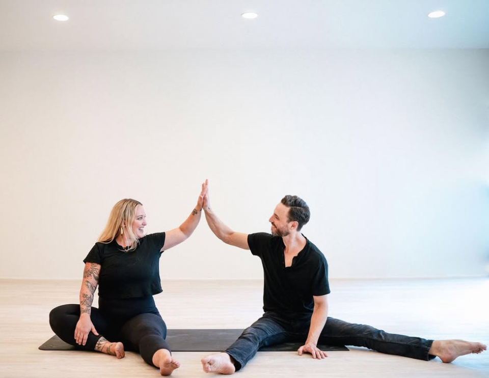 Two people sitting on the floor giving each other a high five in a bright room.