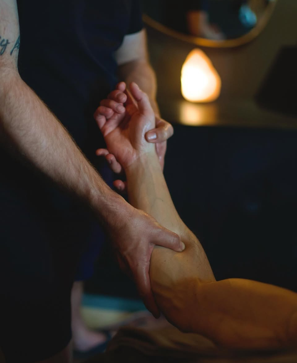 Two people hold hands, one gripping the other's wrist, in a dimly lit room with a glowing lamp in the background.