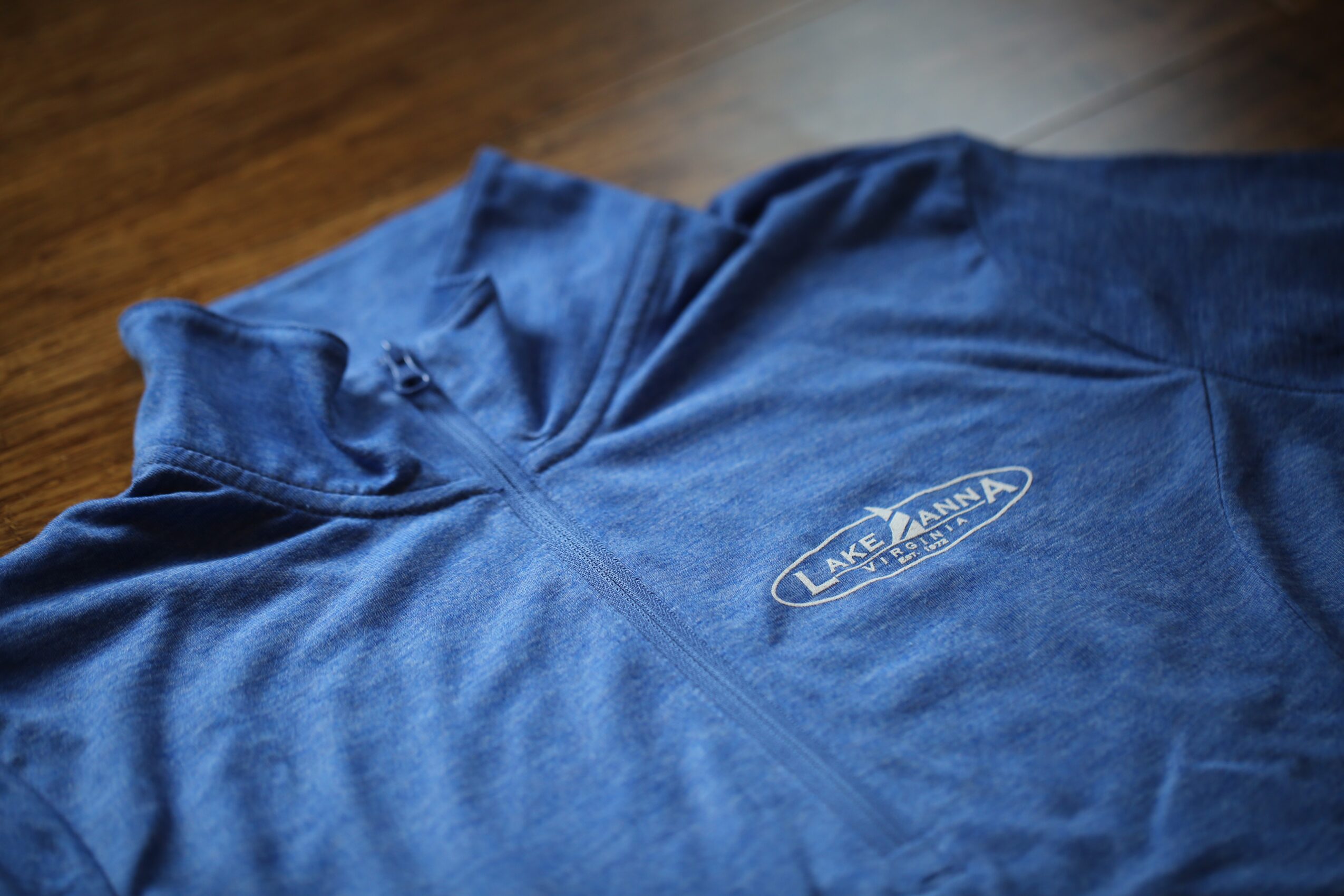 Blue zip-up jacket with a logo on the chest, lying on a wooden surface.