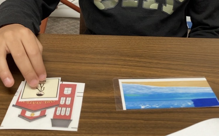 Child's hand reaching for a card on a wooden table, with a landscape photograph nearby.