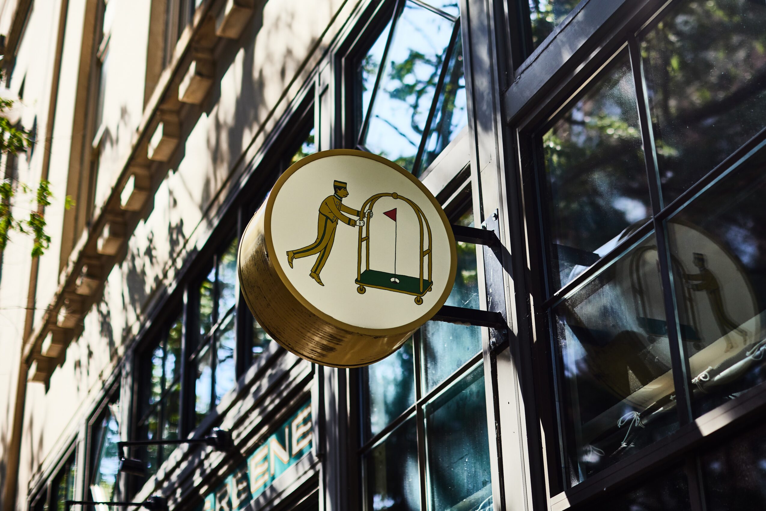 Round sign with a person pushing a cart, mounted on a building exterior with glass windows.