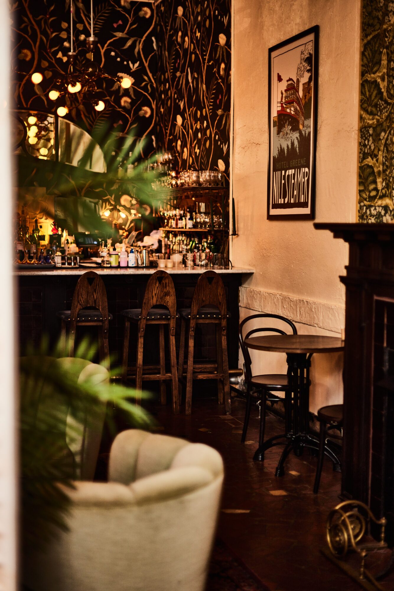 Bar area with wooden stools, a framed picture on the wall, and a cream-colored armchair in foreground.
