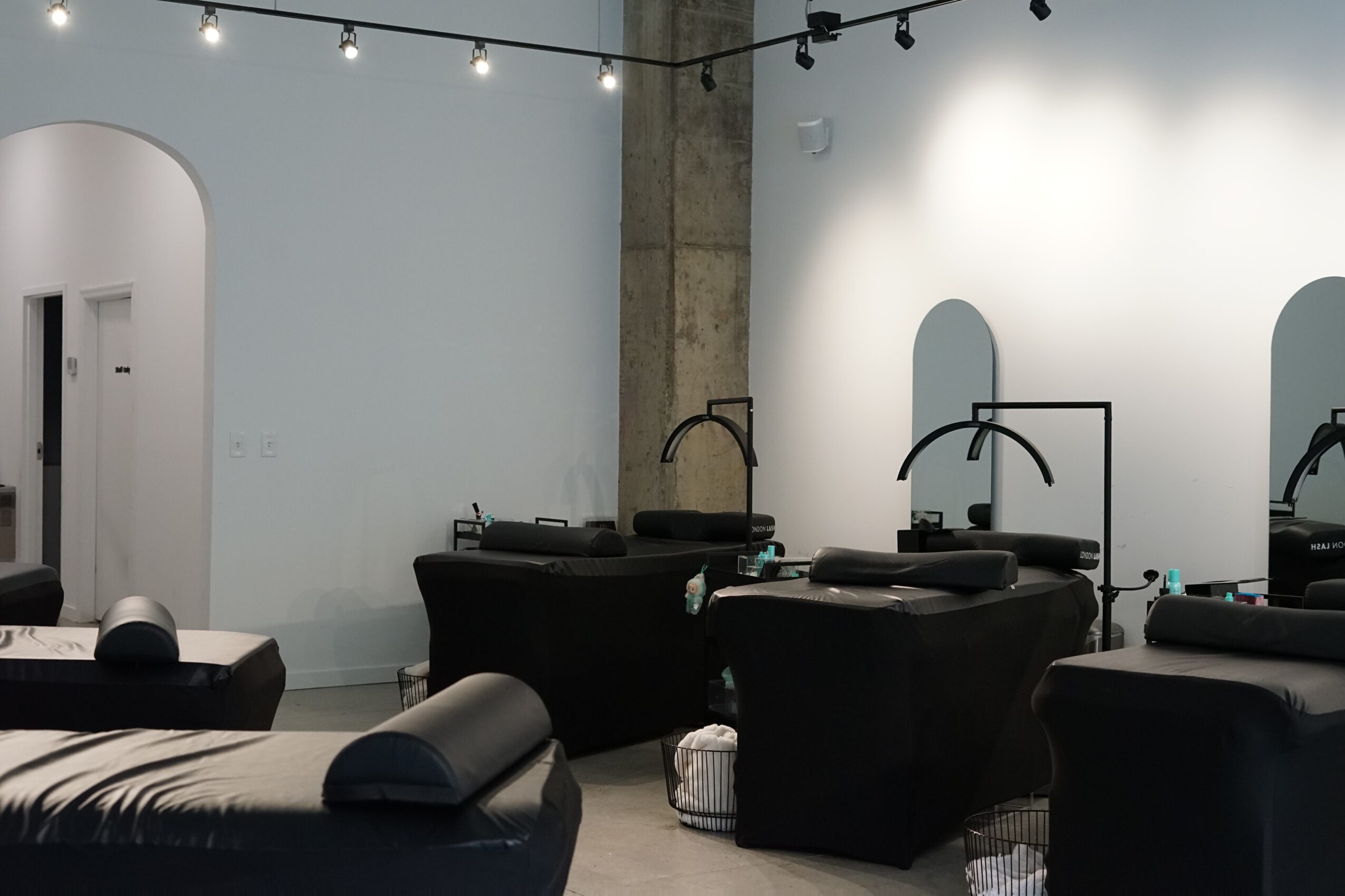 Salon with black chairs, sinks, and mirrors, illuminated by string lights and overhead lighting.