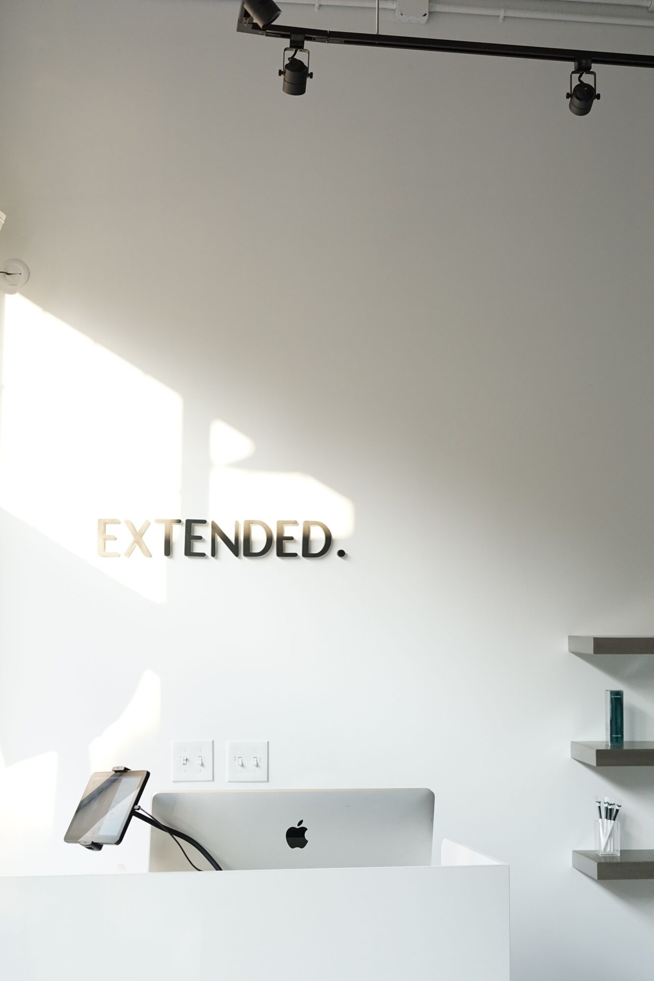 White wall with the word 'EXTENDED' in black and orange, illuminated by sunlight, with electrical outlets and a device on the right.