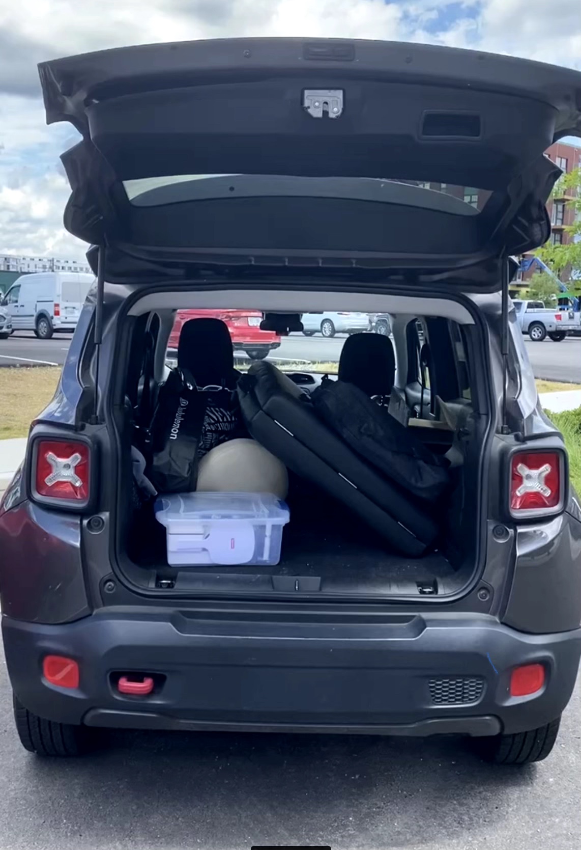 Open car trunk showing golf bags, a cooler, and other items inside, with parking lot and sky in background.